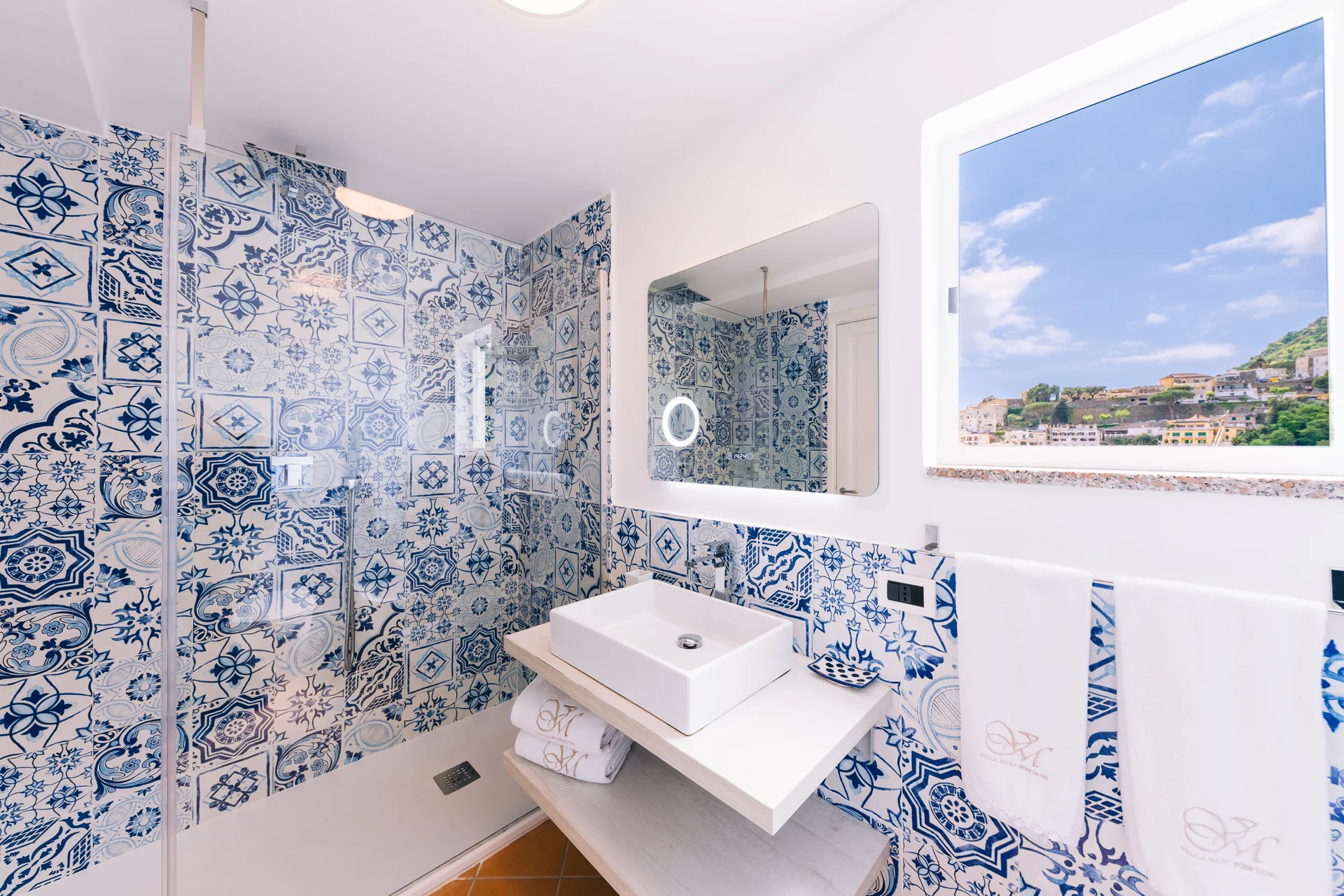 Bagno con maioliche blu, sanitari bianchi e finestra con vista mare